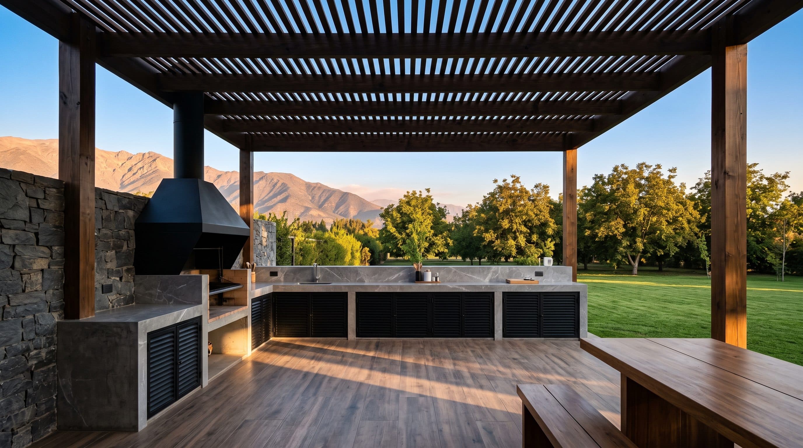 Imagen referencial: quincho bajo pérgola de listones de madera, con mesón de hormigón y vista a la cordillera al atardecer